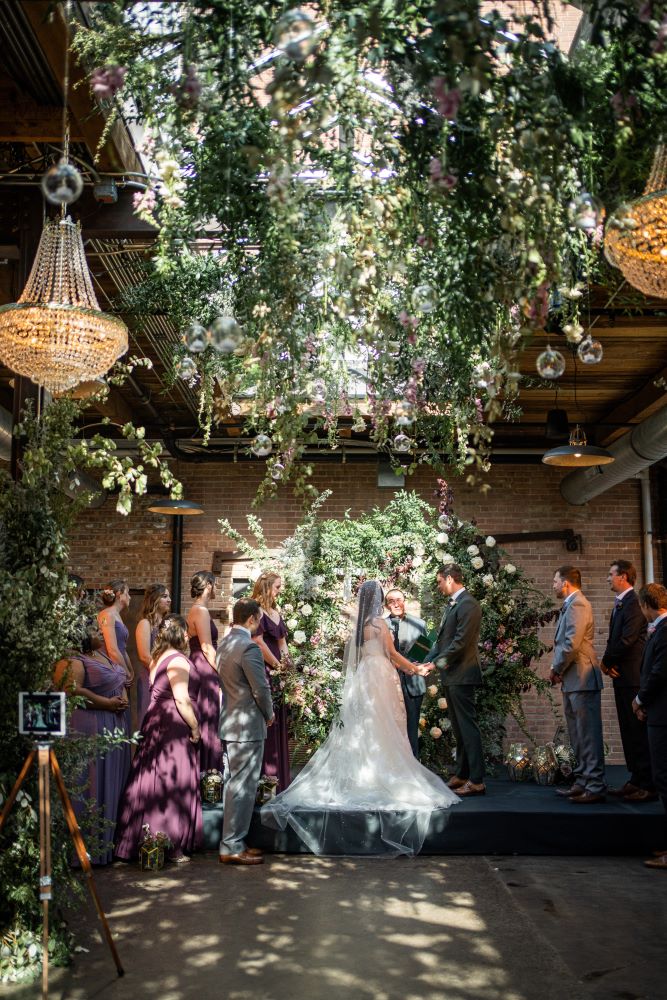 Wedding decor featuring a floral circular ceremony arch, hanging florals, and chandeliers
